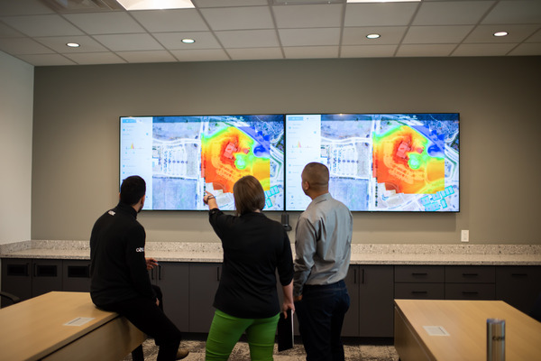 Three coworkers reading a heat map from a large tv screen on the wall
