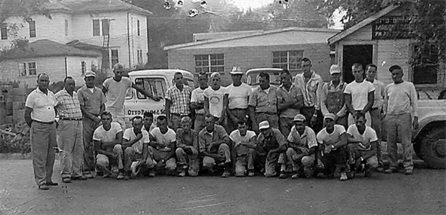Black and white photo of a group of construction workers in the 1940s, standing and kneeling in front of the house.