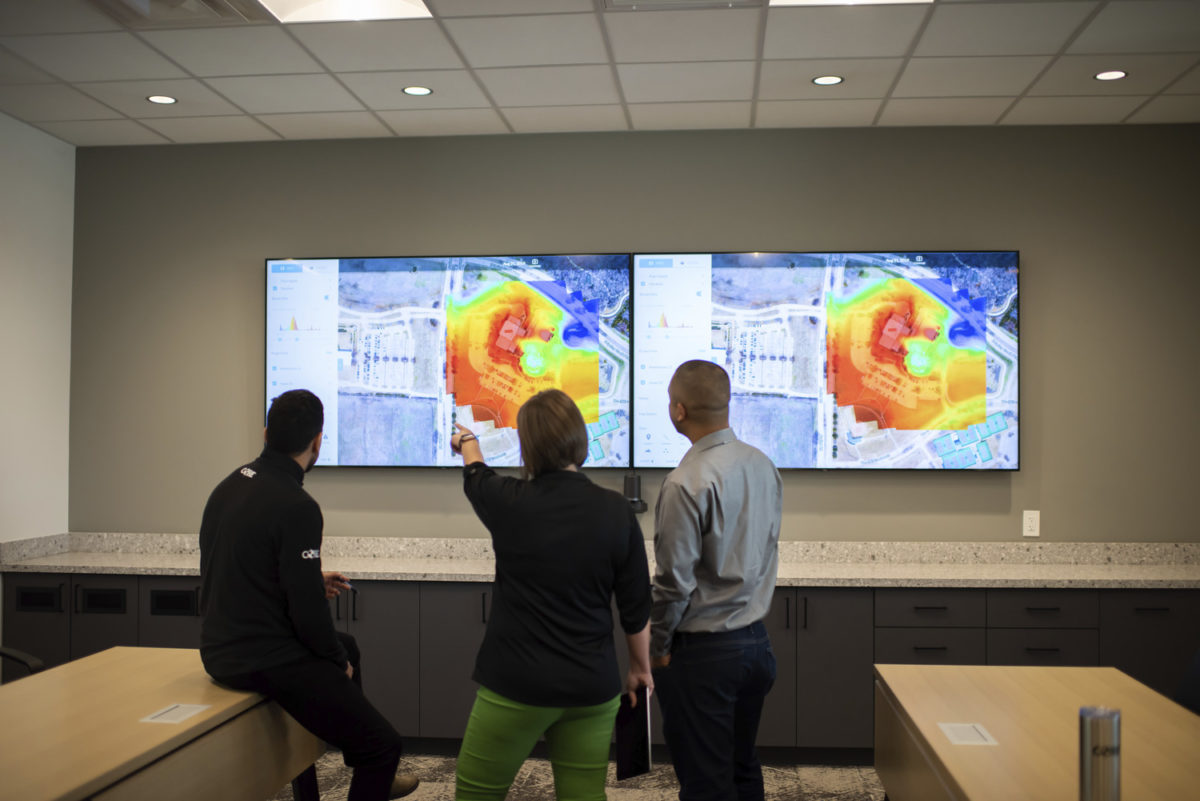Three coworkers reading a heat map from a large tv screen on the wall.