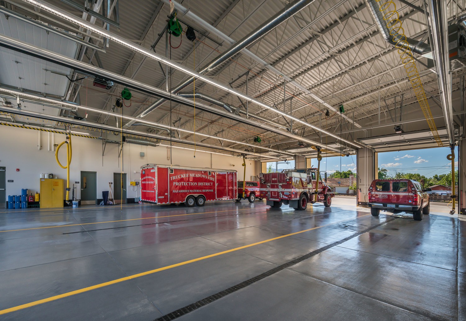 Inside a large fire truck bay showing two red fire SUVs and a red trailer.