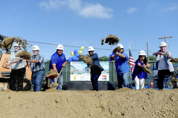 Seven men and women in CORE Construction hard hats hold shovels and toss dirt at a groundbreaking ceremony.
